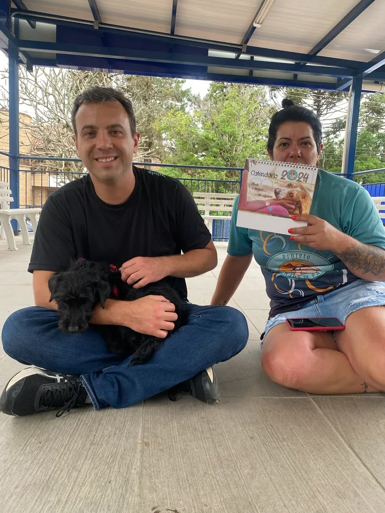 Apoiadores em evento do Projeto Anjos de Patas com cachorro adotado e calendário da causa.